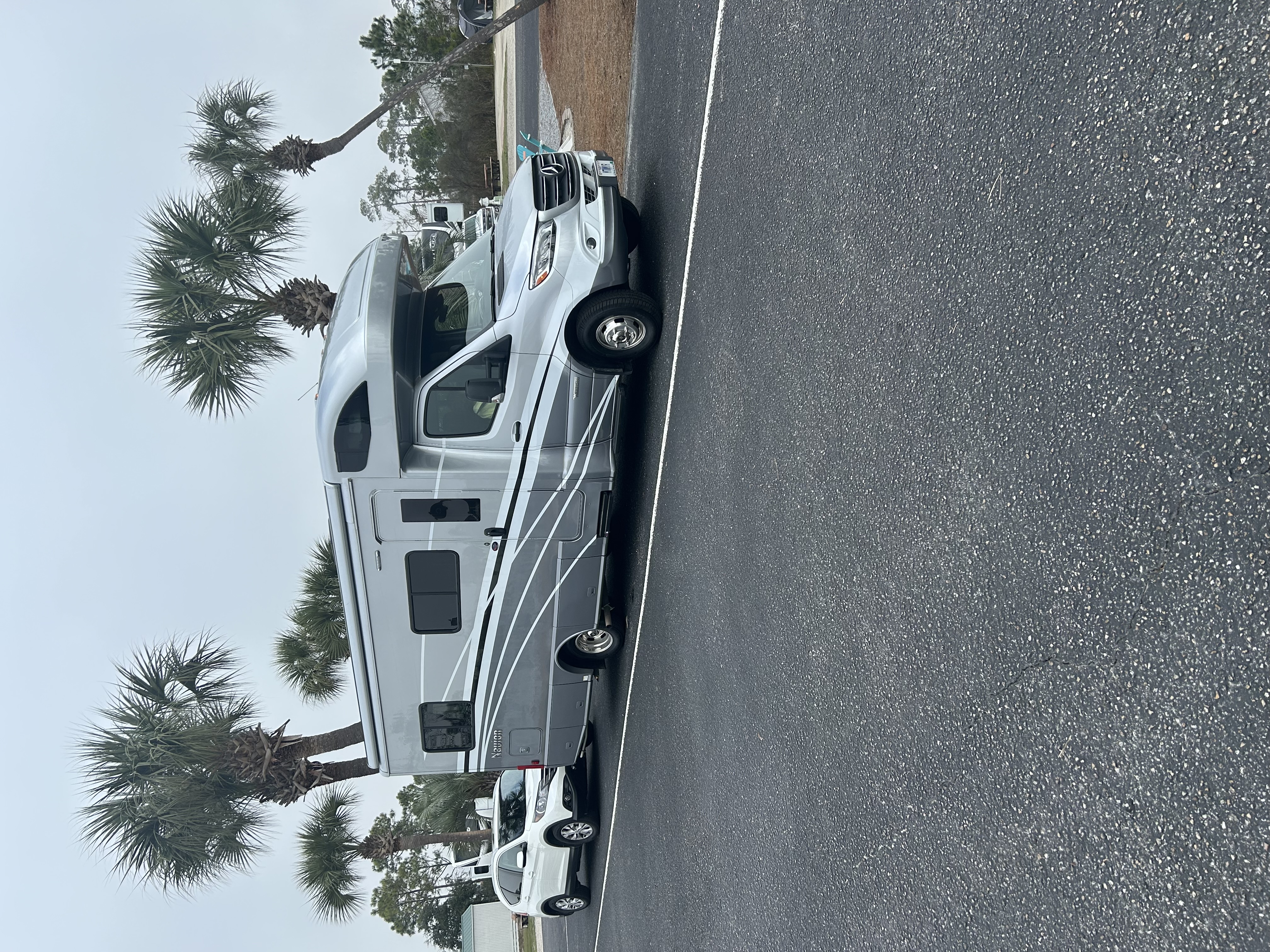 Our silver Winnebago Navion 24V and tow car at a campsite lined with palm trees